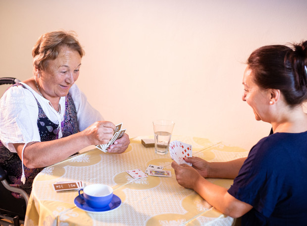 Señora mayor en su domicilio jugando a las cartas con su cuidadora