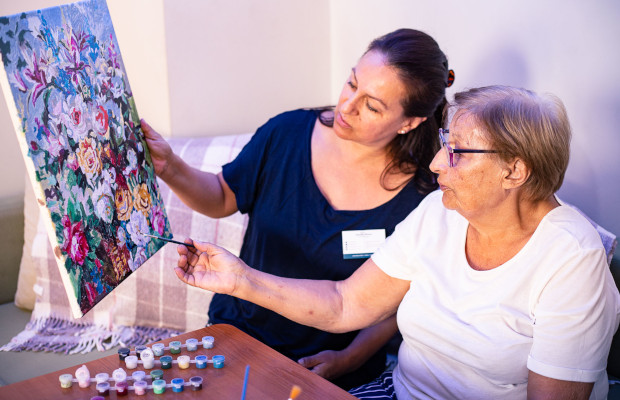 Cuidadora pintando al óleo un cuadro junto a la señora mayor a la que cuida